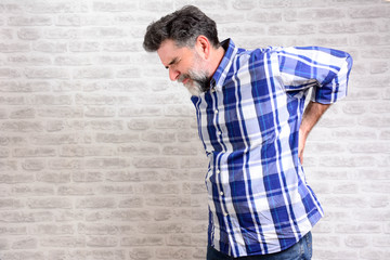 Obraz premium people, healthcare and problem concept - Handsome old man is having back pain at home. Unhappy mature man suffering from backache at home.