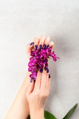 Fototapeta premium Stylish trendy purple female manicure. Woman hands are holding orchid flowers