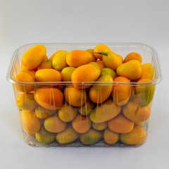 Fresh kumquat fruits in a transparent plastic market container. Isolated.