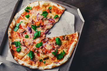 Pizza with Mozzarella cheese, onion, tuna fish, tomato sauce, pepper, basil. Italian pizza in the in delivery cardboard box on wooden table background