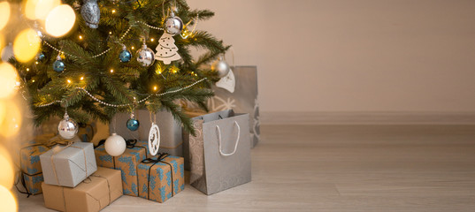 Photo of luxury gift boxes under Christmas tree, New Year home decorations, golden wrapping of Santa presents, festive tree decorated with garland, baubles, traditional celebration