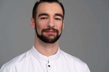 Portrait of a handsome bearded guy in white clothes on a gray background.