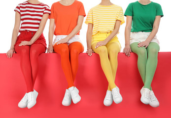 Obraz premium Women wearing bright tights sitting together on color background, closeup