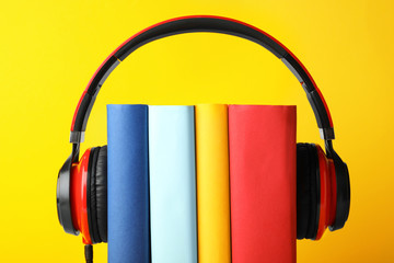 Books with modern headphones on yellow background, closeup