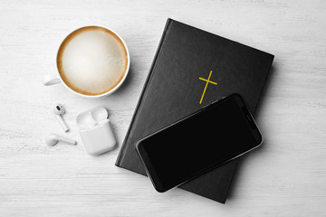 Bible, phone, cup of coffee and earphones on white wooden background, flat lay. Religious audiobook