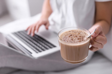 Woman with cup of morning coffee working on laptop indoors, closeup