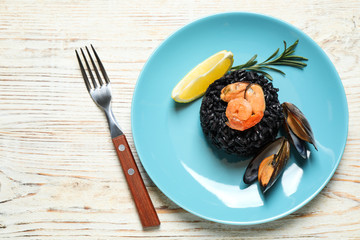 Delicious black risotto with seafood on white wooden table, top view