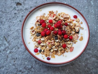 Bowl with yogurt, muesli and lingonberries on grey rough stone texture background.
