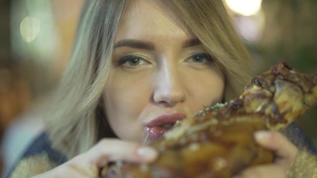 Blonde attractive young greedy woman biting huge pieces of meat eating with hands angry inappropriate in close up shot