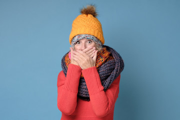 Surprised amazed blonde senior woman having astonished face expression, covering her open mouth with hands, looking at camera in shock and full disbelief