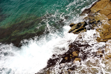 Turquoise sea surface and white sea foam and waves that splashes the stone on the coast