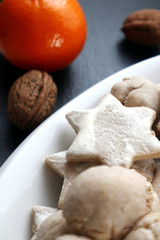 baked cookies in white plate on a dark grey slate with mandarin and nuts