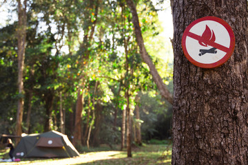 Fire danger sign on the tree. Icon of prohibition of fire risk at the woods. It is forbidden to light a fire on a camping tent at a Natural Park. Stop burning nature resources. Prevent deforestation