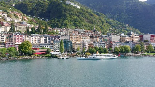 Lateral aerial shot of Swiss excursion ship at Montreux on Lake Geneva shoreline. Flag of Switzerland fixed to the stern of boat. View to Grand Montreux Hotel