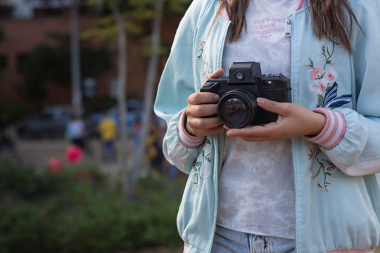 Joven mujer sosteniendo su camara en las manos mientras hace fotografia en el parque
