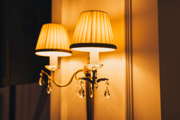 Sconce, wall lamp glows on the background of the wall. An expensive, modern chandelier with glass decorations for the bedroom. Photography, concept, subject.