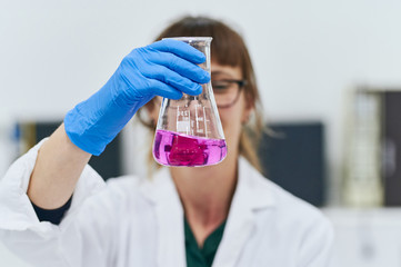 Front view portrait of young woman looking at a pinky liquid in an erlenmeyer flask. Female...