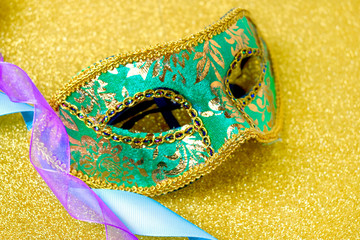 Close up green carnival mask with  purple, blue ribbons on sparkle background. Mardi gras or festive Venice carnival concept.