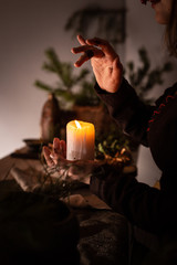 A woman dressed in a medieval dress holds a burning white candle in her hand. Mystery witch