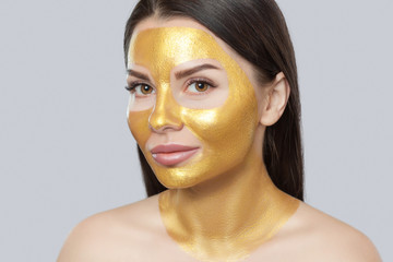Portrait of a brunette woman who makes a golden mask on her face, neck and collarbones against...