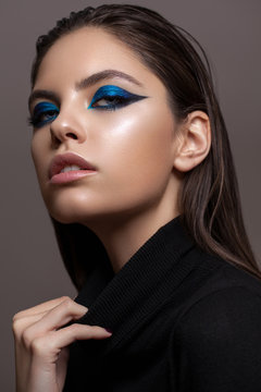 Portrait of a beautiful girl with professional makeup, ideal skin, bright blue graphic smokey eyes and in black sweater