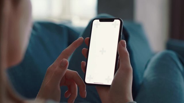 Caucasian woman lying on sofa, relaxing and scrolling her smartphone or mobile phone or cell phone with vertical green white screen. Over shoulder shot, close-up, slow motion. Shoot on ARRI ALEXA.