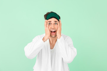 Screaming man in bathrobe and sleep mask on color background