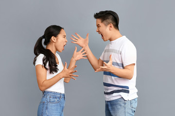 Quarrelling Asian couple on grey background