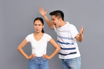Quarrelling Asian couple on grey background
