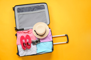 Suitcase with packed clothes and photo camera on color background