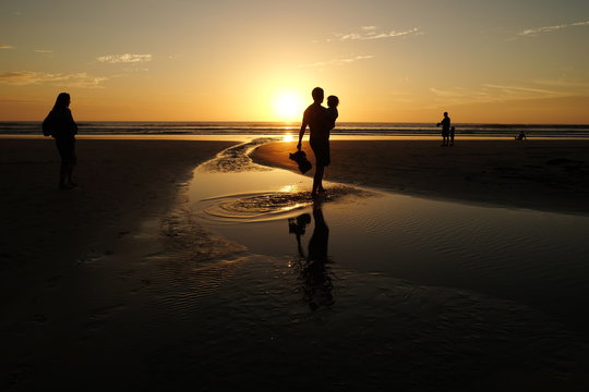 Silhouettes of people by the beach in Costa Rica, watching the sunset, light reflecting tide pool in the foreground of the picture