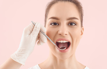 Dentist examining teeth of beautiful young woman against color background