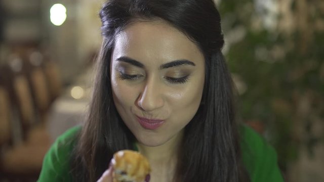 Attractive brunet young female consuming eating custard pastry dessert with dirty hands in fancy restaurant in close up