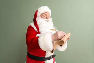 Fototapeta na wymiar Santa Claus making list of gifts on color background