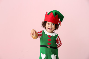 Little girl in costume of elf and with Christmas ball on color background