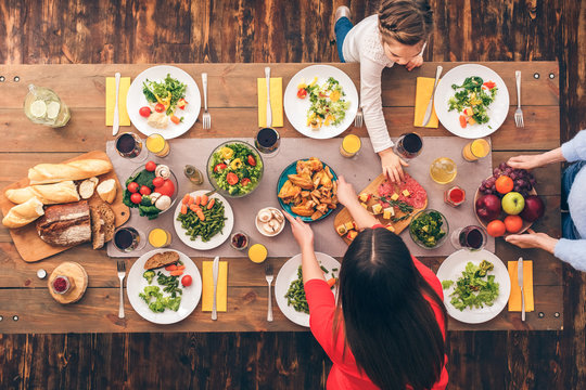 Young Woman And Her Daughter, Grandma Putting Food On Table