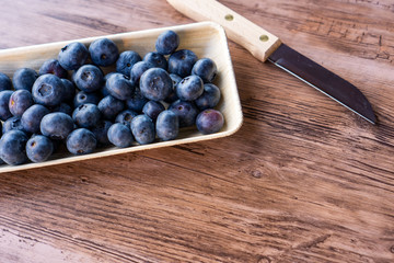 blueberries in a bowl of palm leaves and a knife on a kitchen table