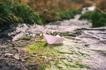 Papierboot in einem Bach als Metapher für Freiheit, Sehnsucht und turbulente Zeiten
