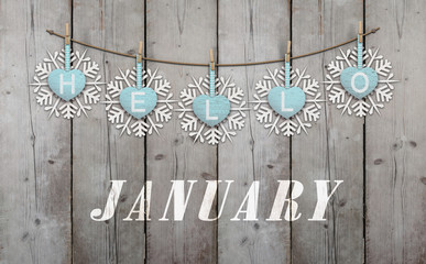 Hello january written on hanging ice blue hearts and white wooden snowflakes on weathered planks background