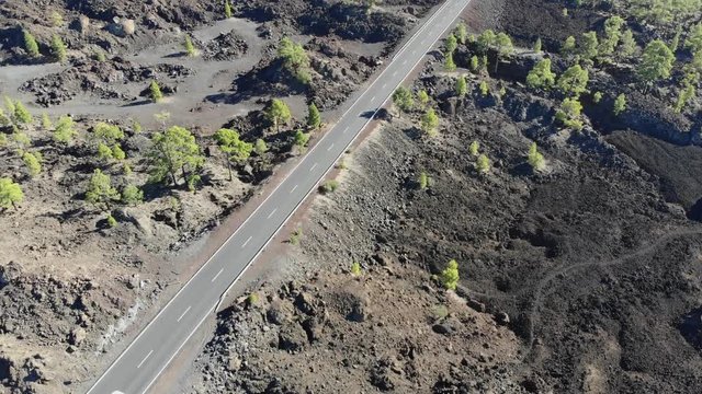 Aerial view: cars driving of road through beautiful volcanic landscape and black rocks, solidified lava flows. 4K drone footage during sunny day. Volcano Teide, Tenerife, Canary islands, Spain
