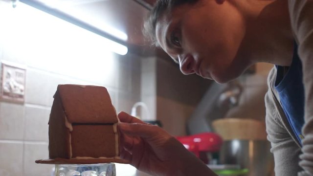 Footage of caucasian woman decorating a homemade gingerbread house for christmas with sugar icing