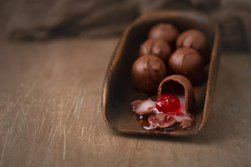 Chocolate covered cherries in brown scoop.  One isolated in front.  Brown background.