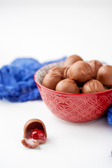 Pretty red bowl of chocolate covered cherries on white background.  Blue fabric.  White background with room for text. One open and isolated in front of bowl.
