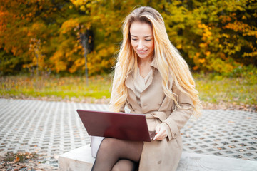 Young sensitive woman using laptop computer outdoor in the park. Freelance work concept. Learning...