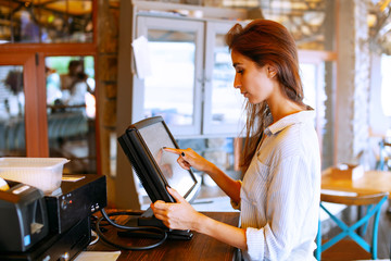 Close-up view of waitress registrated orders to the payment terminal. Young and beautiful waitress stand near sale terminal and check the order.