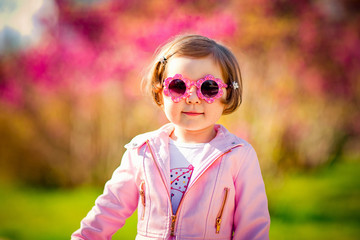a small, beautiful girl in pink clothes and sunglasses, walking in the Park
