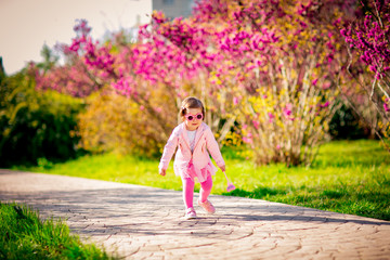 a small, beautiful girl in pink clothes and sunglasses, walking in the Park