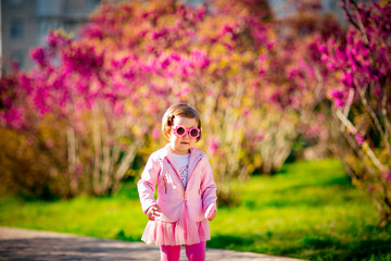 a small, beautiful girl in pink clothes and sunglasses, walking in the Park