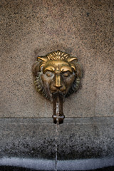 Old venetian fountain with lion heads springs pure drinking water in SOFIA BULGARIA August 12, 2019. Close up stone fountain bowl and mouth of a golden lion fountain. selective focus