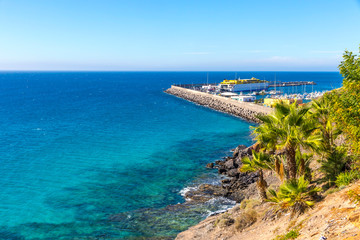 Azure water of Atlantic ocean on Morro Jable beach, Fuerteventura island, Canary Islands, Spain. Port of Morro Jable  in a distance - obrazy, fototapety, plakaty